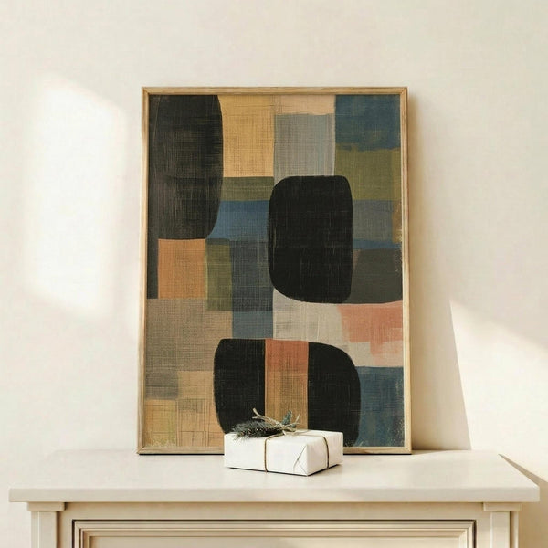 May include: Abstract geometric artwork in wooden frame leaning against white wall on light wood surface, featuring overlapping rectangular and rounded shapes in black, sage green, coral, navy blue, beige and gray with textured brushstroke effects. Small white wrapped gift box with natural twine and greenery sprig sits in front of the framed piece.