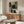 May include: Abstract geometric artwork displayed above walnut credenza in modern living room. Poster features overlapping rounded rectangles and squares in muted tones of sage green, dusty blue, coral pink, cream and black on textured background. Room styled with curved white chair, brass floor lamp, oval glass coffee table and white table lamp.