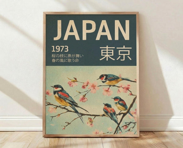 May include: Framed vintage-style travel poster with dark green header and cream background, featuring four colorful birds perched on cherry blossom branches with pink flowers, displayed against white textured wall on light wood floor with natural lighting creating soft shadows