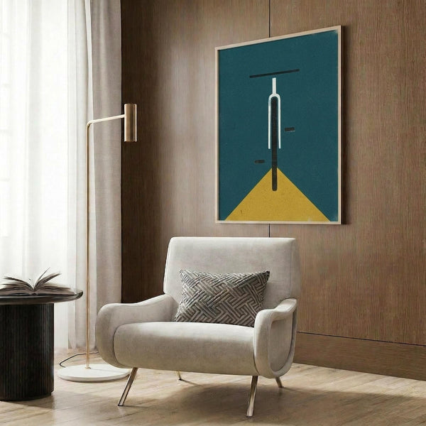 May include: Modern living room with beige armchair displaying framed minimalist bicycle poster. Artwork features white bicycle silhouette on teal background with yellow triangle base, mounted on wood paneled wall. Scene includes brass floor lamp, patterned throw pillow, and dark side table with open book.