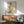 May include: Framed Japanese art print featuring a woman in mint green kimono with coral obi sash and red hair ornament, holding a katana sword, displayed on white wall above wooden sideboard with ceramic table lamp and mid-century modern sage green armchair in sunlit room