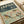 May include: Vintage-style poster featuring colorful birds perched on cherry blossom branches against pale green background, with "JAPAN" and "1973" text in dark teal header, displayed on white surface alongside rolled paper and neutral fabric materials in soft natural lighting.