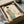 May include: Japanese-style artwork in black frame showing woman in flowing green and coral kimono holding red katana sword, with bamboo leaves in background. Framed print sits in cardboard shipping box with protective wrapping, surrounded by white tissue paper on neutral surface.