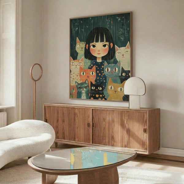 May include: Framed artwork showing a young girl with black bob haircut surrounded by multiple colorful cats in various shades of orange, gray, white, and black against a dark green rainy background. The illustration has a whimsical, folk art style. The frame sits on a mid-century modern wooden credenza beside a white mushroom lamp and cream colored chair, with an oval glass coffee table in the foreground.