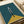 Minimalist geometric artwork on teal and mustard yellow background featuring abstract white and black linear shapes resembling a simplified bicycle front view. The print is displayed flat on white paper with a cream ribbon visible in the corner, showing the artwork's clean lines and modern color palette against the neutral backdrop.