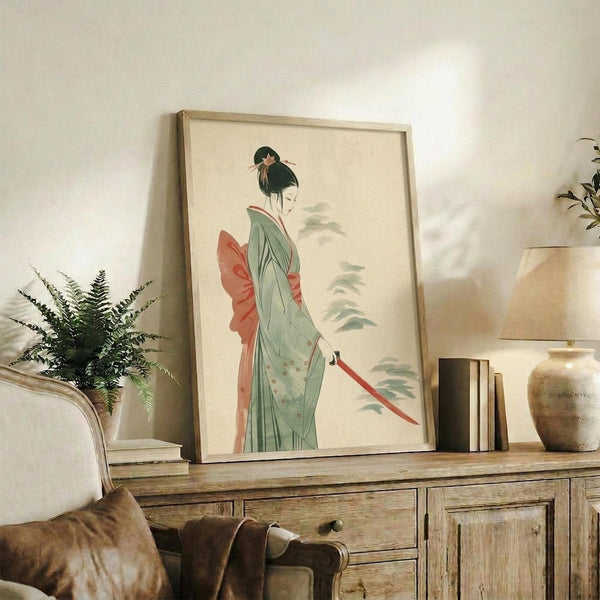 May include: Framed art print displayed on rustic wooden console table showing Japanese woman in flowing green kimono with coral obi sash, holding red katana sword. Soft watercolor style with muted background. Scene includes fern plant, ceramic vase, stacked books, and cream upholstered chair in warm-toned living room setting.