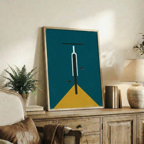 May include: Framed geometric poster with teal background featuring minimalist white and black bicycle handlebars above yellow triangle, displayed on rustic wooden sideboard alongside fern plant, books, ceramic vase, and brown leather chair in modern living room setting with white walls and soft natural lighting.