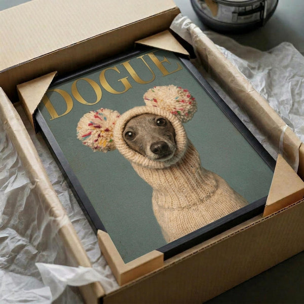 May include: Framed poster print in cardboard shipping box with protective wrapping. Artwork shows Italian Greyhound wearing cream knit sweater and pom-pom hat on sage green background. Gold "DOGUE" text appears above the dog in fashion magazine style. Black frame nestled in brown cardboard packaging with white tissue paper on marble surface.