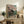 May include: Framed Japanese woodblock print featuring cherry blossoms over traditional temple buildings with small figures below, displayed on rustic wooden sideboard alongside potted fern, ceramic vase, and books in neutral-toned living room setting
