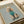 May include: Framed poster print on white bedding showing a cream poodle wearing a turquoise turtleneck sweater and matching socks against a sage green background, with "DOGUE" in gold letters at the top mimicking a fashion magazine cover