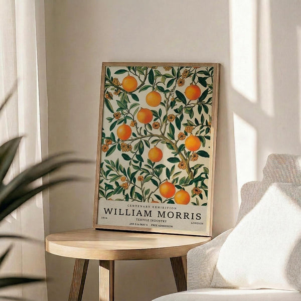 May include: Framed botanical poster featuring orange citrus fruits and green leaves on cream background, displayed on round wooden side table next to beige upholstered chair. Natural sunlight streams across white walls creating soft shadows. Plant leaves visible in corner of bright, minimalist living room setting.