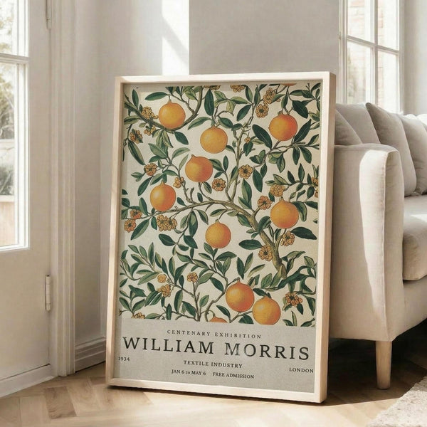 May include: Large framed poster with botanical design featuring orange citrus fruits and green foliage on cream background, displayed against white wall next to beige upholstered sofa in bright living room with tall windows. Natural wood frame complements the vintage-style artwork with exhibition text at bottom.
