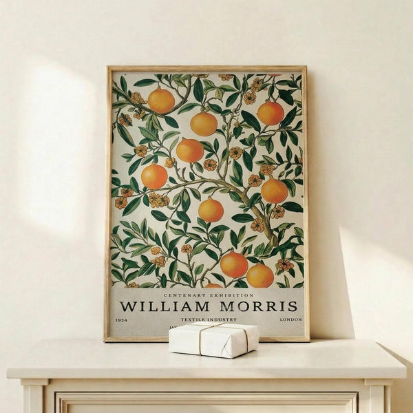May include: Framed botanical poster featuring orange citrus fruits and green foliage in William Morris decorative style, displayed on light wood shelf against cream wall. Natural wood frame surrounds vintage-inspired textile pattern with "WILLIAM MORRIS" and "CENTENARY EXHIBITION" text at bottom. Small white decorative object sits beside frame.