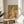 May include: Framed art print displayed on round wooden side table next to beige upholstered chair. Print features woman with red hair in low bun wearing cream dress with brown leaf pattern, surrounded by orange and peach flowers against sage green background. Natural lighting creates soft shadows across neutral-toned room setting with plant visible in corner.