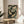 May include: Vintage Japanese art print featuring two golden koi fish swimming among lotus flowers and lily pads on dark water background, displayed in thin wooden frame on round wooden side table next to beige upholstered chair, with plant shadows and natural window light creating soft ambiance in neutral-toned room setting.