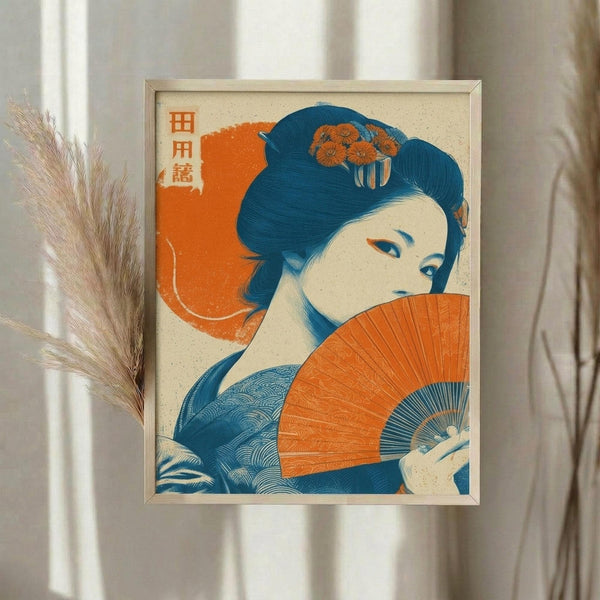 May include: Framed Japanese-style art print displayed on white wall beside dried pampas grass. Artwork features woman in traditional dress holding orange folding fan, rendered in blue and orange colors with Japanese text characters. Print has cream background with light wooden frame, shown in soft natural lighting with neutral curtains visible.