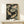 May include: Framed Japanese-style artwork showing two golden koi fish swimming among pink lotus flowers and green lily pads on a dark background, displayed on a light wood console table next to a small white wrapped gift with greenery accent against a cream wall.