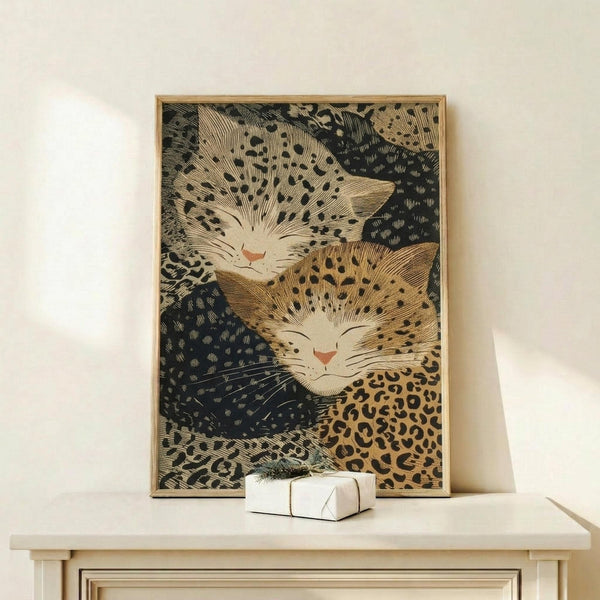 May include: Framed vintage Japanese woodblock print featuring two sleeping cats with spotted leopard-like patterns in warm browns and blacks, displayed on light wood console table beside small white wrapped gift. Art shows detailed line work and traditional ukiyo-e style with cats nestled together against dark patterned background.