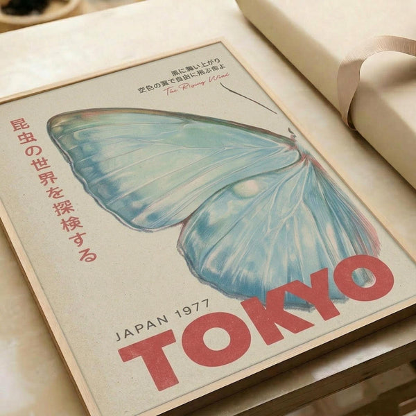 May include: Vintage-style poster print featuring large blue butterfly wings with delicate veining and spots, displayed in an open book or magazine. Red Japanese text runs vertically along the left side, with "JAPAN 1977" and "TOKYO" in bold red letters at bottom. The illustration has a soft, hand-drawn quality with pale blue and white wing colors against cream paper background.