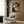 May include: Japanese woodblock print style artwork featuring two spotted leopard cats with closed eyes in golden tones against dark blue background, displayed in light wood frame on textured wall panel above beige upholstered chair with geometric pillow, brass floor lamp and dark side table with open book nearby
