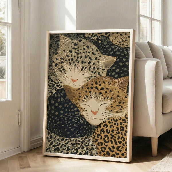 May include: Framed vintage Japanese woodblock print featuring two stylized cats with leopard-spotted fur and radiating whiskers against a dark textured background. The artwork displays traditional ukiyo-e style with golden brown and black tones. Print is shown in a light wood frame leaning against white walls in a bright living room with beige sofa and large windows.