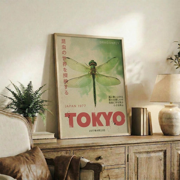 May include: Framed vintage-style poster featuring green dragonfly illustration with Japanese text and red "TOKYO" lettering, displayed on rustic wooden sideboard next to fern plant, books, ceramic vase, and beige armchair in warm-toned living room setting