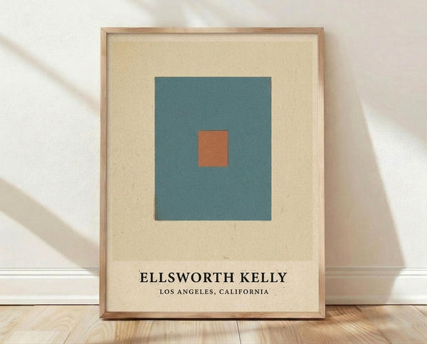 May include: Framed minimalist art print featuring a teal square with small orange square in center on cream background, displayed in light wood frame against white textured wall on wooden floor with soft natural lighting and shadows
