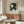 May include: Framed Japanese art poster featuring geometric umbrellas in dark green and cream tones displayed above a mid-century modern wooden credenza. White sculptural chair and glass coffee table complete the minimalist room scene with neutral walls and natural lighting.