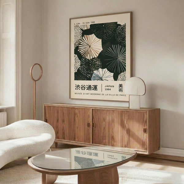 May include: Framed Japanese art poster featuring geometric umbrellas in dark green and cream tones displayed above a mid-century modern wooden credenza. White sculptural chair and glass coffee table complete the minimalist room scene with neutral walls and natural lighting.
