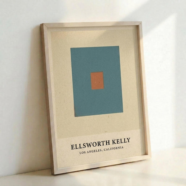 Minimalist art print featuring a teal blue rectangle with small orange square in center on cream background, displayed in light wood frame leaning against white wall with soft natural lighting