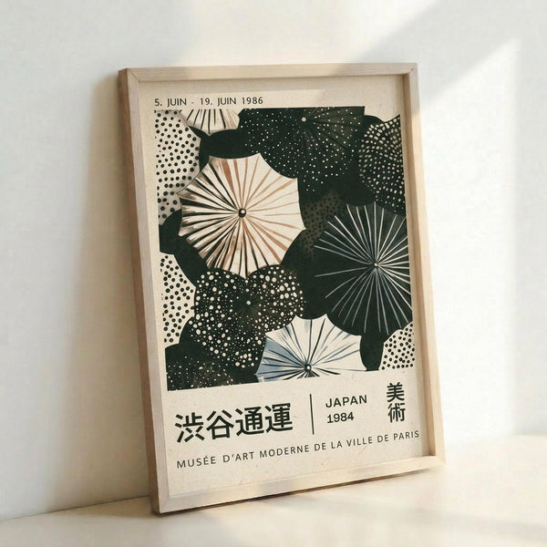 May include: Framed vintage Japanese exhibition poster leaning against white wall, featuring abstract pattern of paper umbrellas and parasols in dark green and cream colors with dotted textures, displayed in light wooden frame, museum poster from 1984 with Japanese text and Paris museum credit at bottom