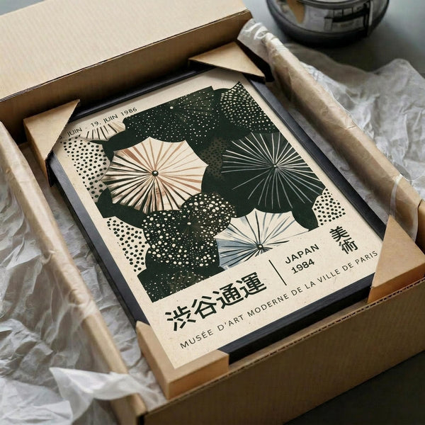 May include: Vintage-style poster featuring Japanese umbrellas in cream, dark green, and muted blue tones with dotted patterns and radiating spoke designs, displayed in black frame inside cardboard shipping box with protective tissue paper wrapping on neutral surface.