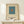 May include: Framed minimalist art print featuring a teal blue square with small orange square in center on cream background, displayed on light wood console table next to small wrapped gift with evergreen sprig, against white wall with natural lighting
