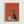 May include: Framed poster print displayed on white wall featuring stylized black cat with wide eyes sitting on wooden surface next to white coffee pot and small cup against vibrant orange-red background, shown in light wood frame with minimal modern room setting