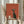 May include: Person holding framed vintage-style poster with orange-red background featuring stylized black cat with large white eyes sitting beside coffee pot and cup on wooden shelf. Light wood frame, dried pampas grass visible, neutral beige clothing and curtains in soft natural lighting.