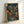 May include: Framed poster print leaning against white wall showing atmospheric Japanese alleyway scene at night with warm glowing lanterns, traditional wooden buildings, stone steps leading upward, and wet cobblestones reflecting light. Artwork features deep blue and teal evening tones contrasted with golden yellow illumination from paper lanterns and shop signs with Japanese characters. Natural wood frame surrounds the detailed illustration in anime or manga art style.