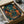 May include: Framed poster print showing atmospheric Japanese street scene at night with warm glowing lanterns, traditional architecture, wet stone steps, and rich teal and orange color palette. Black frame nestled in cardboard shipping box with white tissue paper protection on wooden surface.