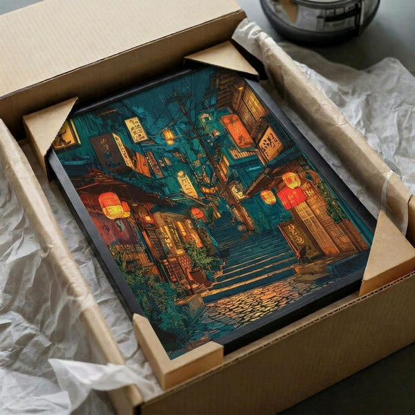 May include: Framed poster print showing atmospheric Japanese street scene at night with warm glowing lanterns, traditional architecture, wet stone steps, and rich teal and orange color palette. Black frame nestled in cardboard shipping box with white tissue paper protection on wooden surface.