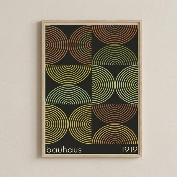 May include: Framed geometric art print with concentric circles in earth tones - browns, greens, and yellows arranged in a grid pattern against dark background. The circles have radiating lines creating a retro, mid-century modern aesthetic. Print shows "bauhaus 1919" text at bottom. Light wood frame hangs on white textured wall.