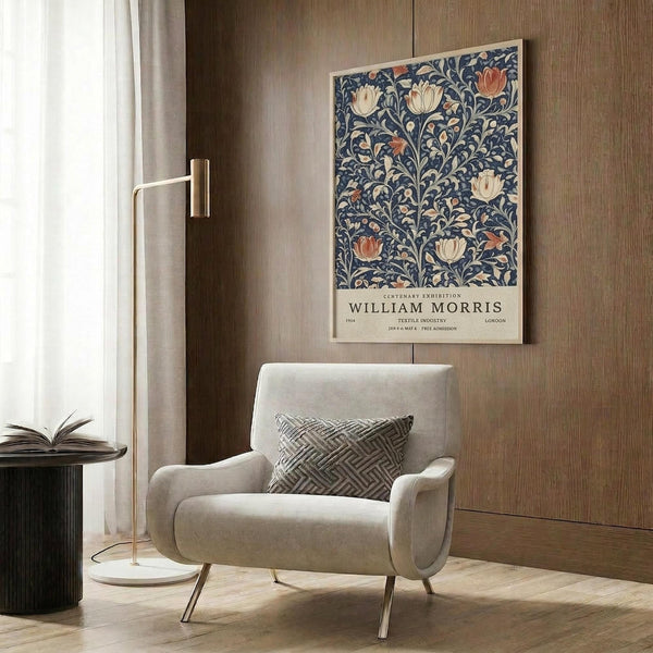 May include: Framed William Morris botanical poster with blue background and cream, orange tulip florals hanging on wood-paneled wall above beige upholstered armchair with geometric pillow. Modern brass floor lamp and dark round side table with open book complete the neutral-toned reading nook with curtained window.