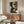 May include: Abstract geometric poster with dark green and cream colored curved and angular shapes displayed above a wooden sideboard in a modern living room setting with white upholstered chair, glass coffee table, and table lamp