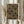 May include: Person holding framed geometric poster featuring overlapping semicircular patterns in warm earth tones of orange, green, and burgundy on dark background. Light wood frame, cream matting, displayed against soft neutral curtains with dried pampas grass visible to the side.