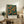 May include: Framed vintage-style botanical poster featuring orange fruit tree with lush green foliage against deep blue background, displayed on rustic wooden sideboard alongside potted fern, ceramic vessels, and stacked books in warmly lit living room with beige upholstered furniture and neutral walls.