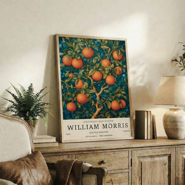May include: Framed vintage-style botanical poster featuring orange fruit tree with lush green foliage against deep blue background, displayed on rustic wooden sideboard alongside potted fern, ceramic vessels, and stacked books in warmly lit living room with beige upholstered furniture and neutral walls.