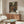 May include: Japanese anime poster featuring colorful illustration of people in traditional clothing on bustling street with lanterns and shops, displayed in thin wooden frame above walnut credenza. Modern living room setting with white curved chair, oval glass coffee table, and cream walls. Warm natural lighting creates shadows across furniture.
