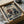 May include: Framed poster artwork displayed in wooden box with tissue paper packaging. The print features two anime characters sword fighting amid stylized ocean waves in traditional Japanese art style. One warrior wears red and white clothing, the other blue robes. Japanese text appears at top. The artwork uses cream, blue, and earth tone colors with dynamic action poses. Wooden dowels visible in packaging materials.
