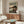 May include: Framed anime poster showing samurai character with sword in red jacket against bridge landscape, displayed above wooden sideboard in modern living room with white curved chair, glass coffee table, and white table lamp