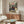 May include: Framed anime poster showing samurai character in red jacket and blue pants wielding sword in mountainous landscape, displayed above wooden sideboard in modern living room with white curved chair, glass coffee table, and warm lighting creating shadows on beige walls.