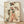 May include: Framed vintage-style Japanese geisha artwork displayed against white wall on wooden floor. The poster shows a geisha in elaborate layered kimono with coral, green, and cream floral patterns, holding a decorative fan. Her black hair is styled in traditional updo with ornamental accessories. The artwork has an aged, weathered appearance with ink splatters and distressed texture on cream background, housed in light wood frame.