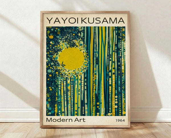 May include: Framed poster print leaning against white wall on light wood floor. The artwork features a bright yellow sun surrounded by stylized forest with vertical tree trunks in teal, green and yellow tones, decorated with dotted patterns and organic shapes. The print has "YAYOI KUSAMA" at top, "Modern Art" and "1964" at bottom in black text on cream background. Natural wood frame visible in warm lighting with soft shadows.